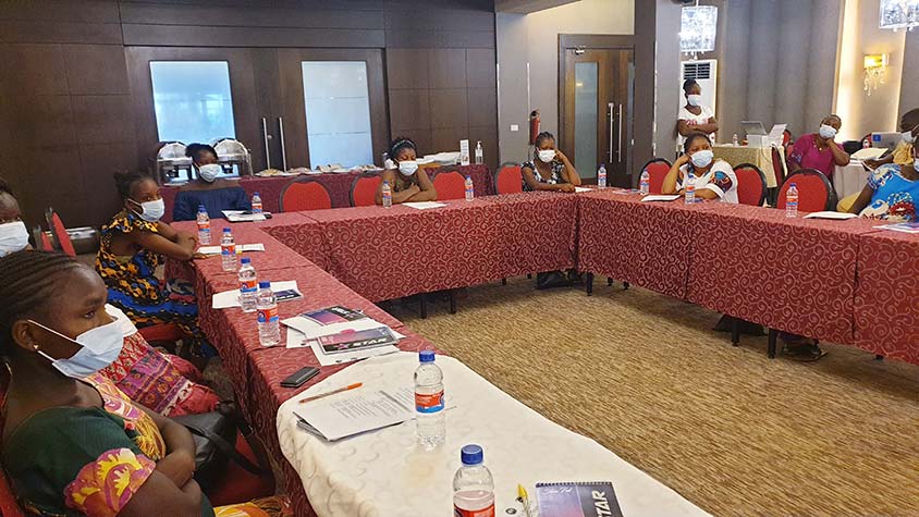 Photo of Liberian women wearing masks sitting at conference tables arranged in a U-shaped formation.