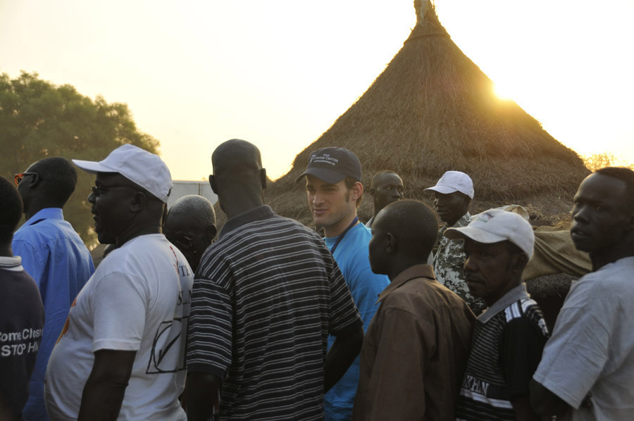 Carter Center observer Owen McDougall talks to voters waiting for voting to begin at Lologo Market polling station.