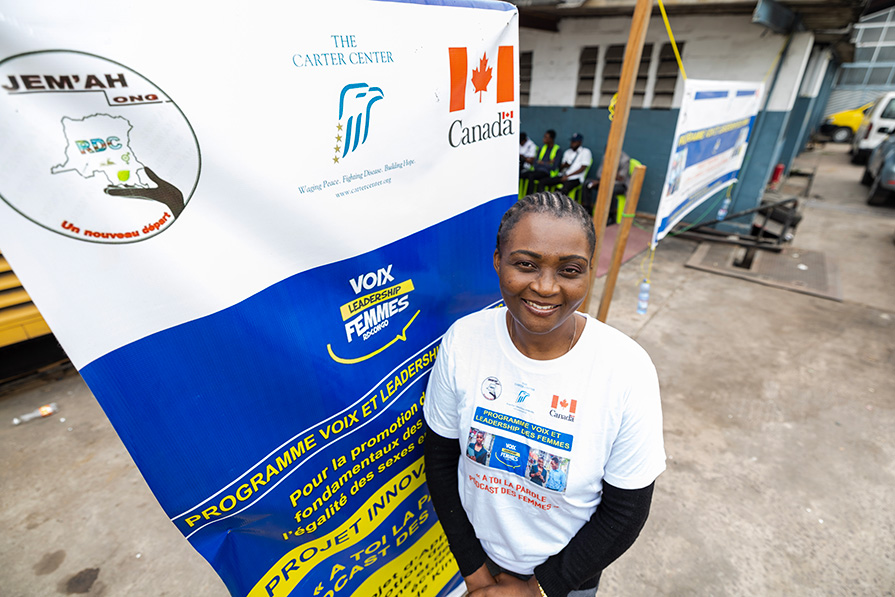 A woman in the DRC stands in front of a sign.