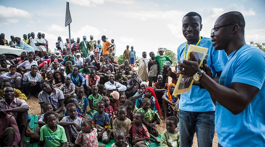 Carter Center technical advisor Laurès Dossou (foreground) and volunteer supervisor Mende Kelmane Alphonso instruct a crowd on how to detect Guinea worm disease during a 2018 cash rewards ceremony in Dangabol Village, Chad. People who report suspected Guinea worm infections and take appropriate measures can receive rewards of up to $100. (Photo: The Carter Center/J. Hahn)