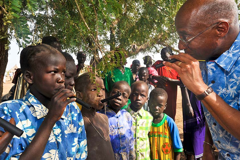 Photo of Dr. Hopkins demonstrating how to use a pipe filter. A group of children look on.